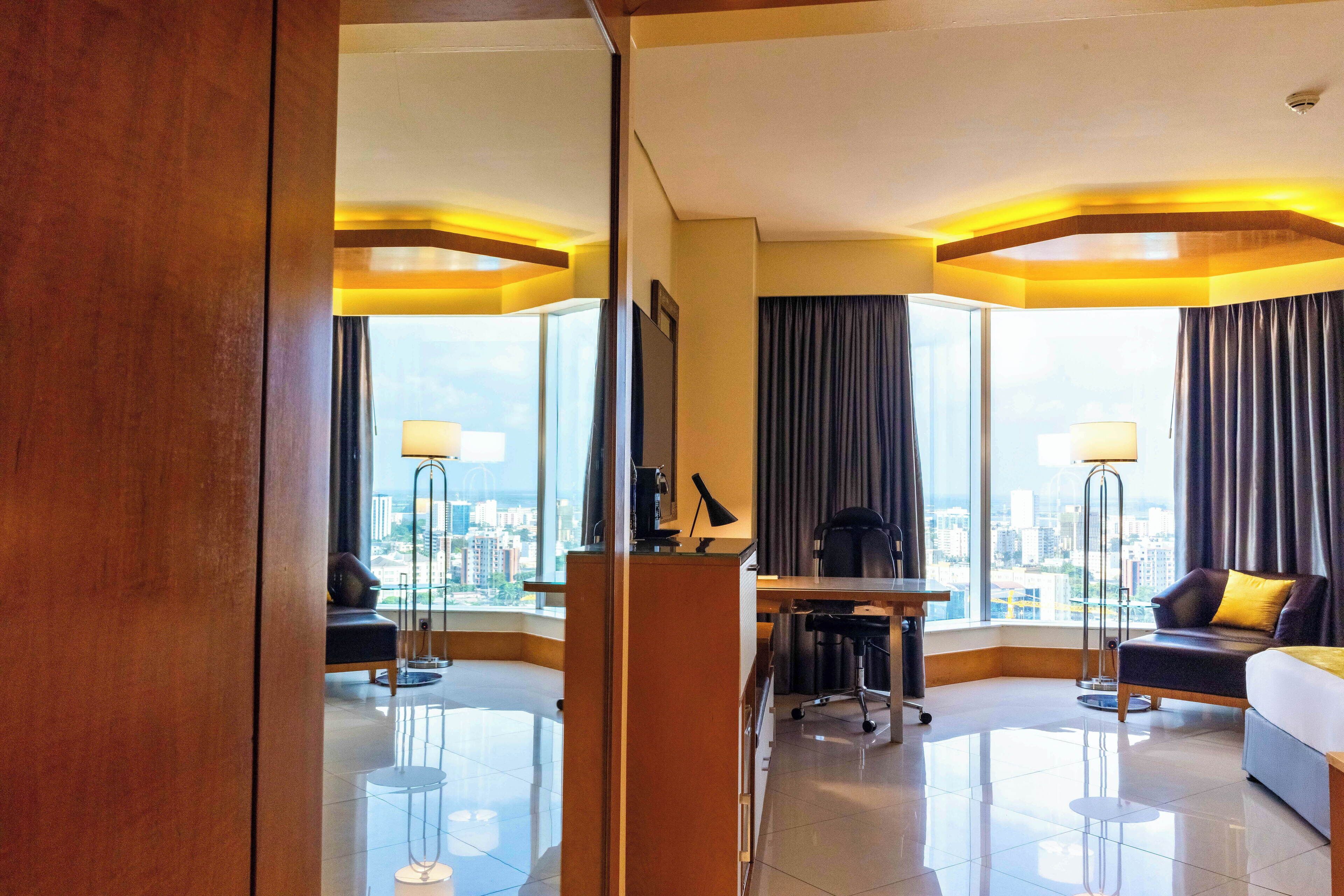 A hotel room with a city view, a desk, a sofa, and a bed.