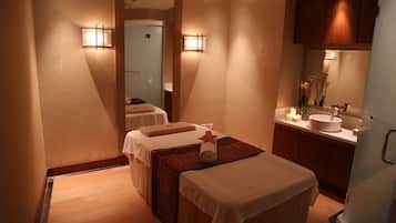 Relax in a serene spa room with two massage tables, a vanity, and a glass shower enclosure.