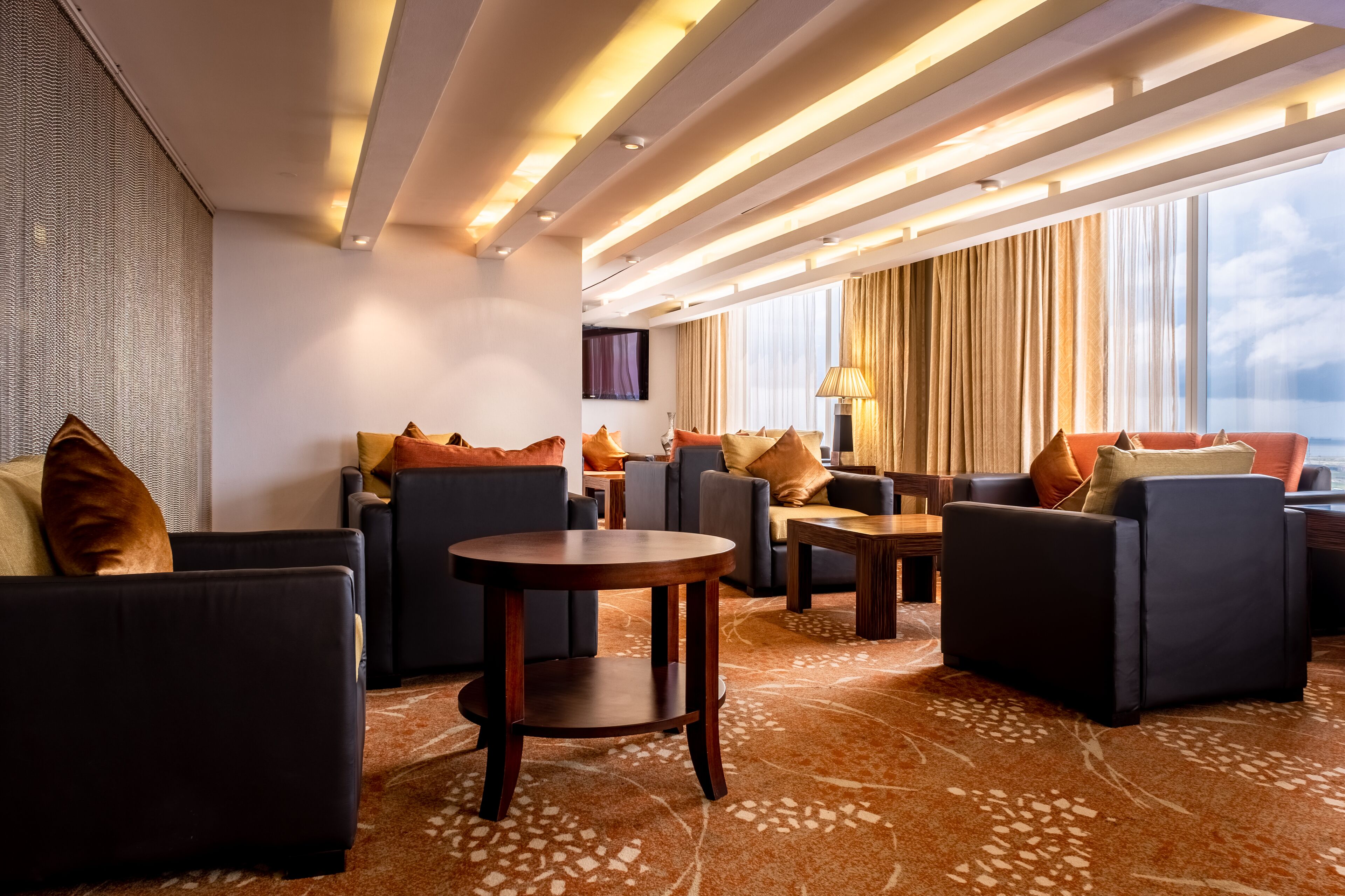 A modern hotel lobby with sofas, a round table, and a large window with curtains.