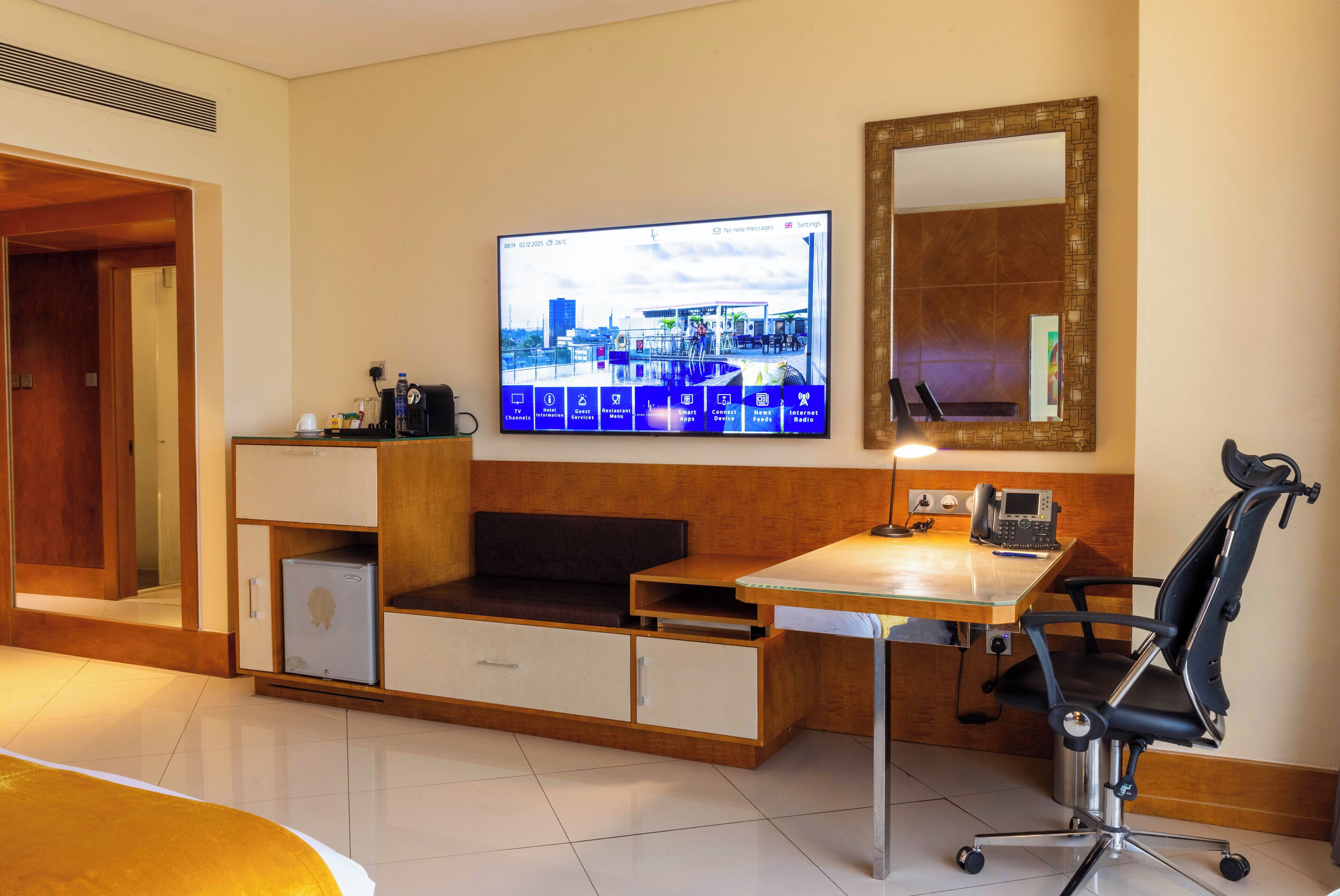 Hotellihuone, jossa on puinen työpöytä, musta toimistotuoli, seinälle asennettu televisio ja peili työpöydän yläpuolella.