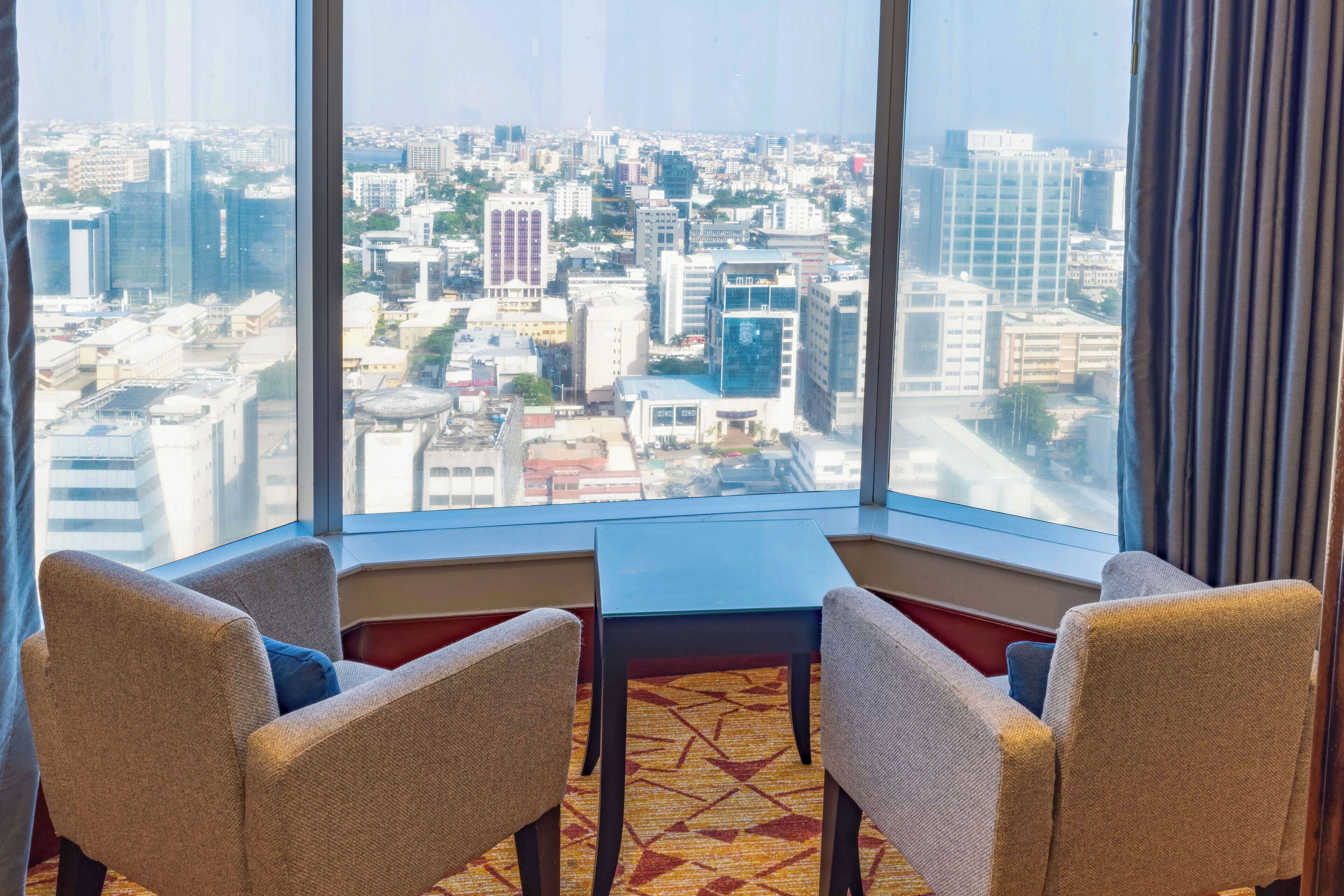 A corner room with two chairs and a small table, large windows with a city view.