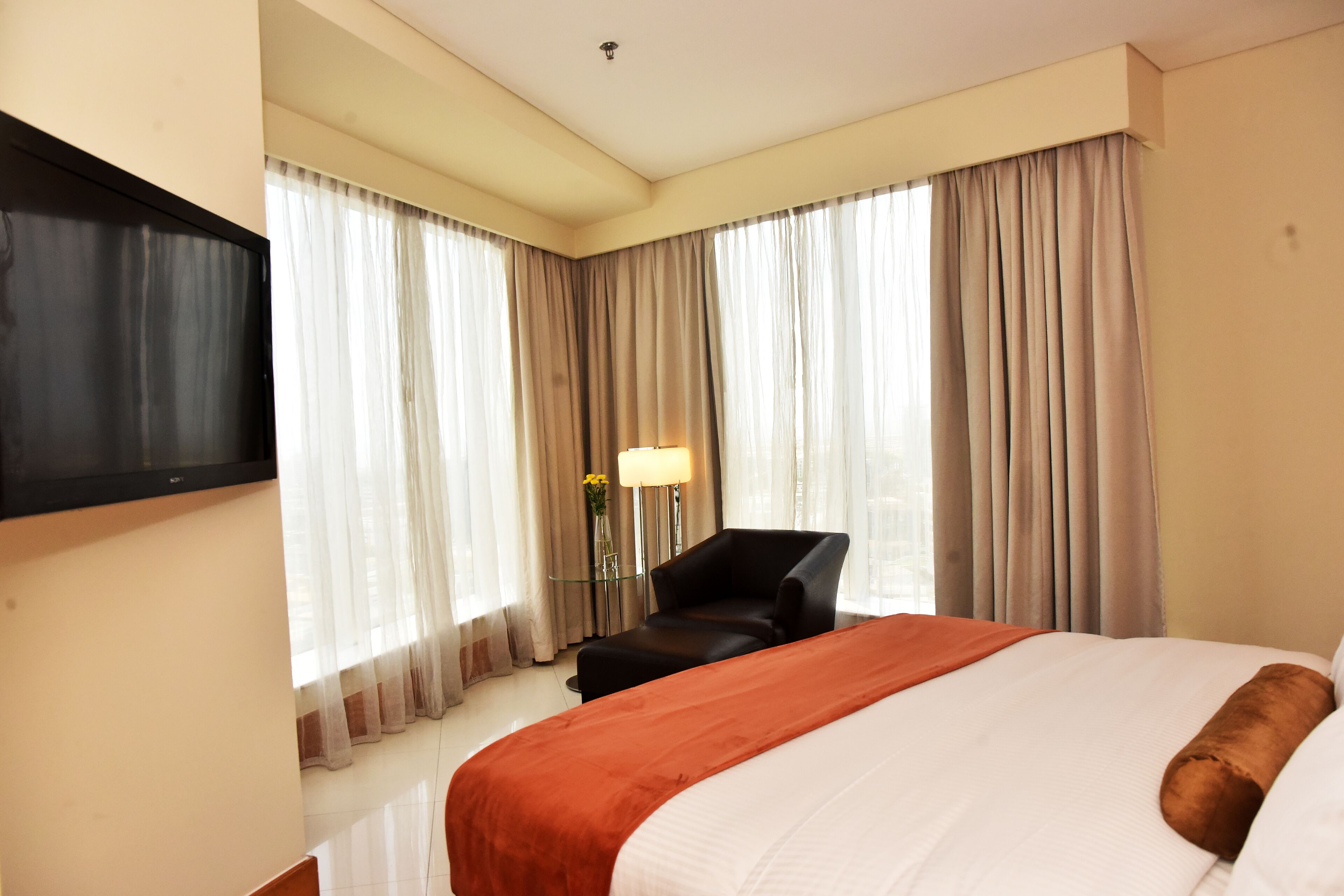 A hotel room with a bed, a TV mounted on the wall, a chair, and a lamp.