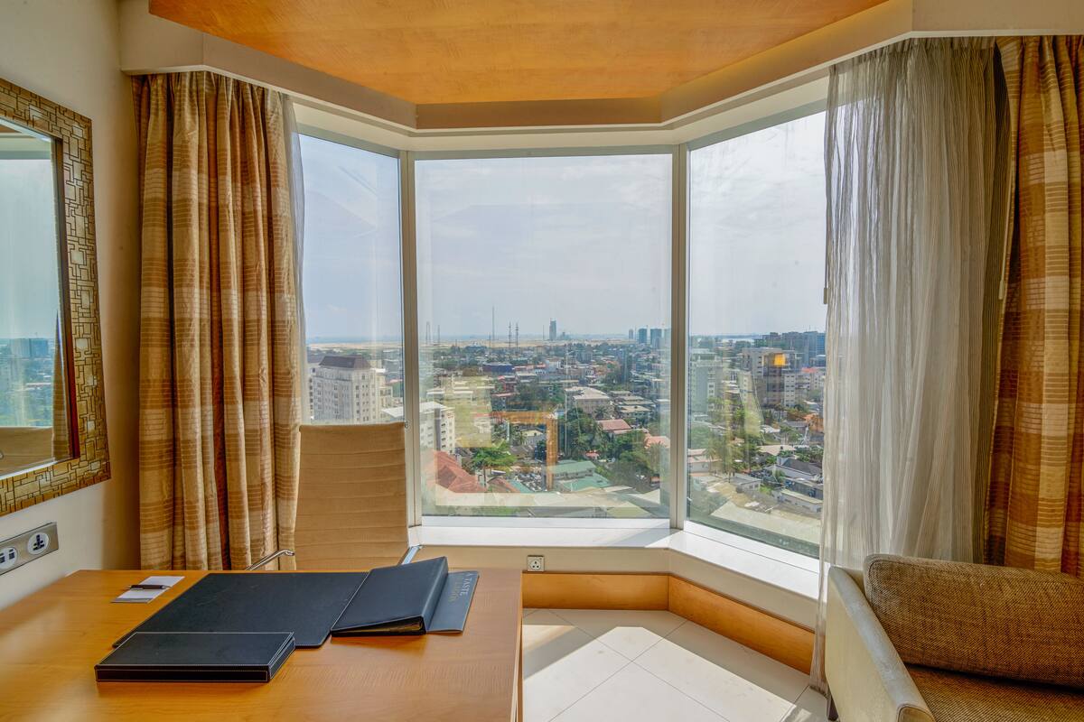 A corner room with a large window, a desk, a chair, and a view of a cityscape.