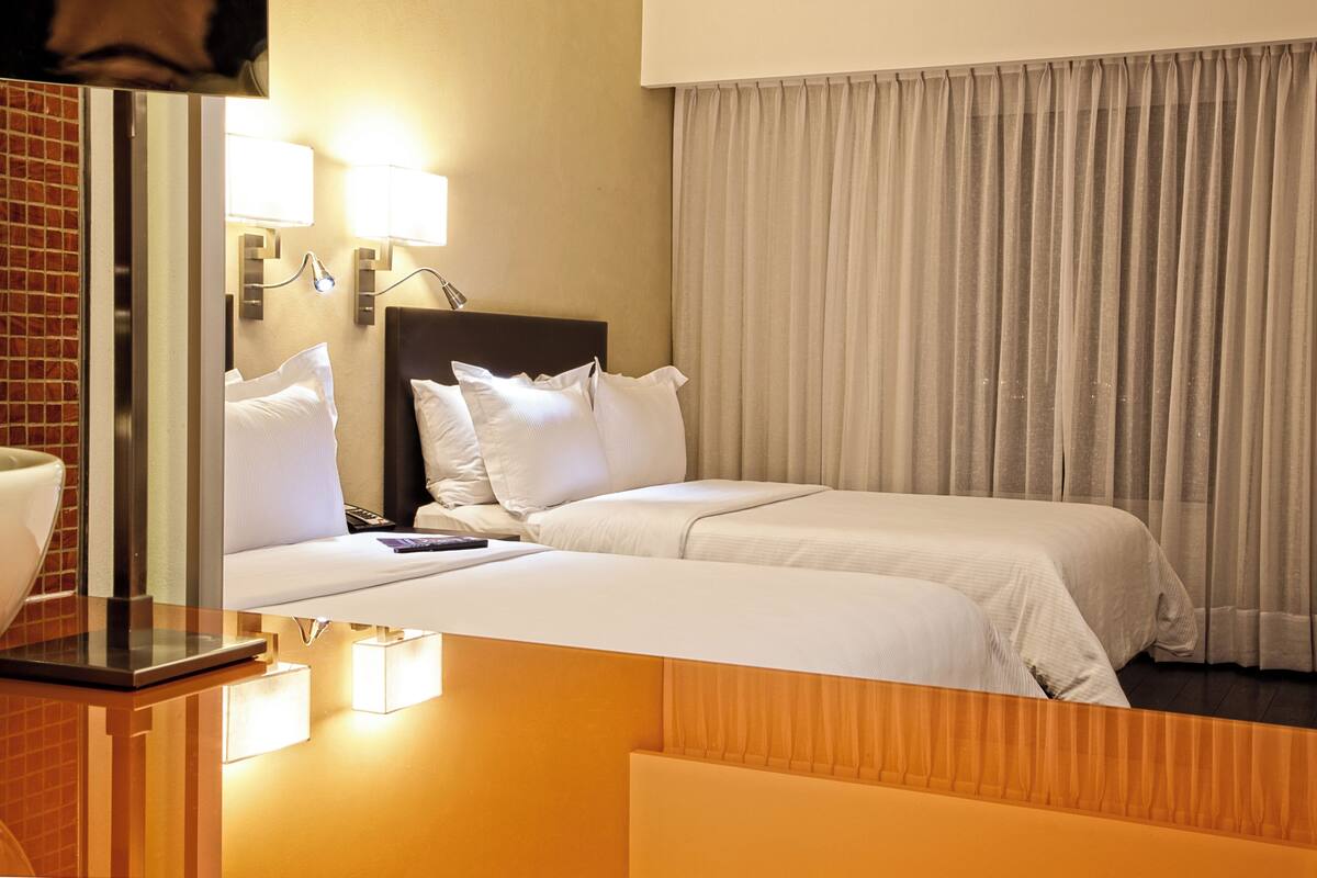 Een hotelkamer met twee bedden, een houten hoofdbord, een spiegel en een nachtkastje.