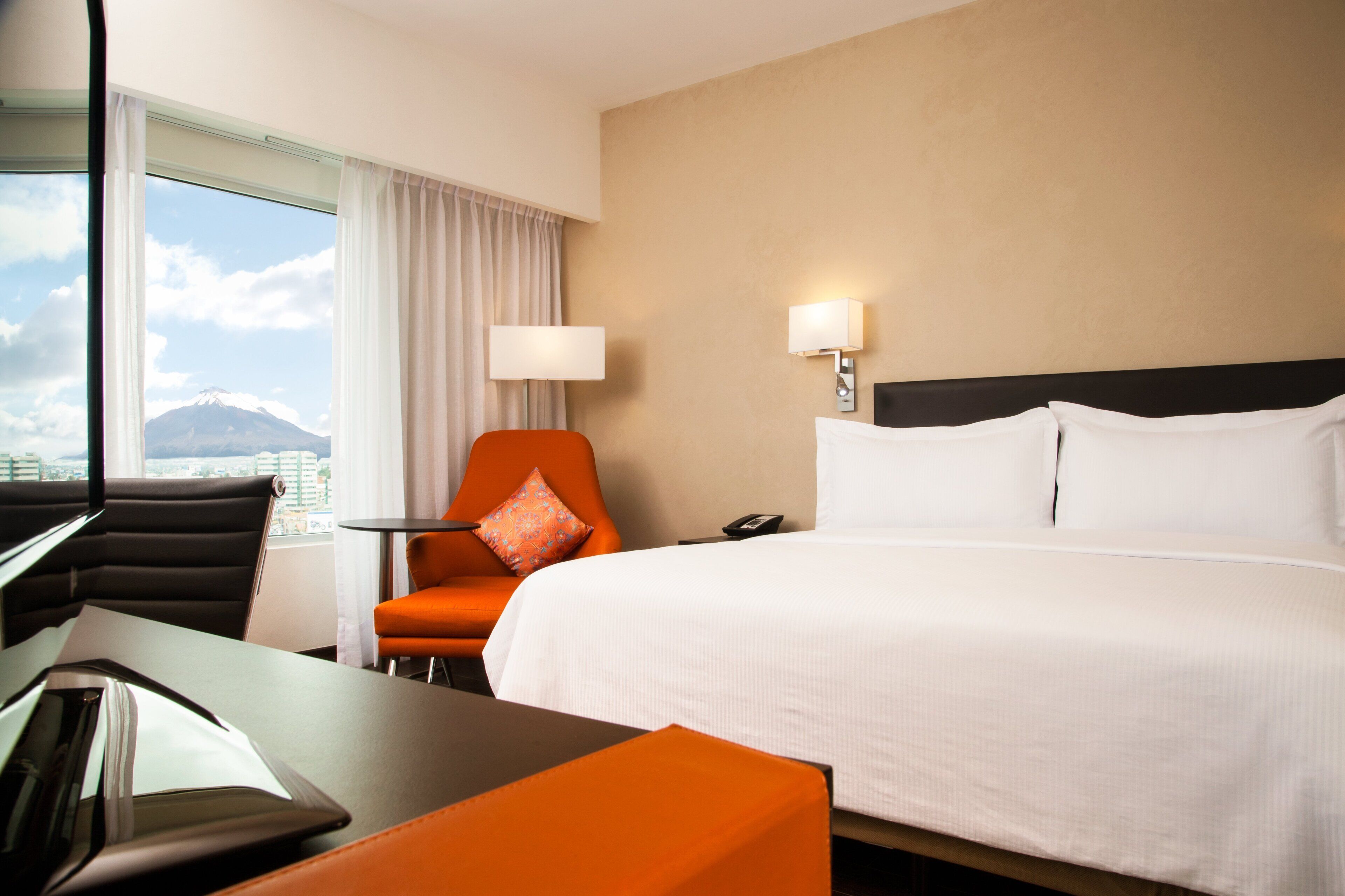 A hotel room with a bed, a desk, a chair, and a view of a mountain.