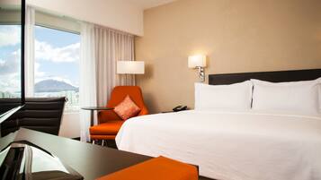A hotel room with a bed, a desk, a chair, and a view of a mountain.