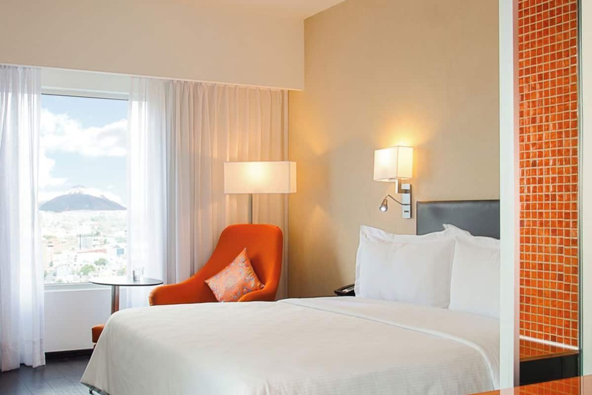 Een hotelkamer met een bed, een stoel, een tafel en uitzicht op een berg.