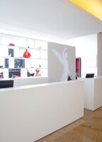 Un área de recepción con un mostrador blanco, estantes con diversos objetos y un gran mural en la pared.