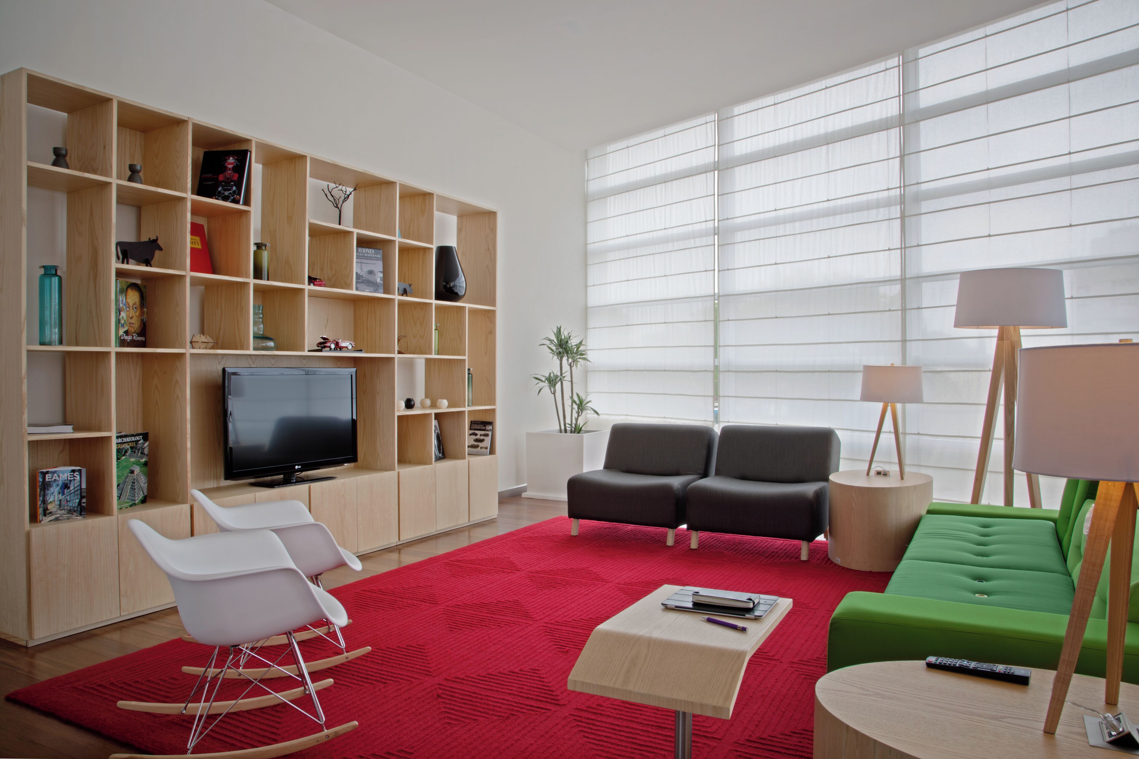 Una sala de estar moderna con un televisor de pantalla plana, una alfombra roja, un sofá verde y una estantería de madera llena de libros y objetos decorativos.