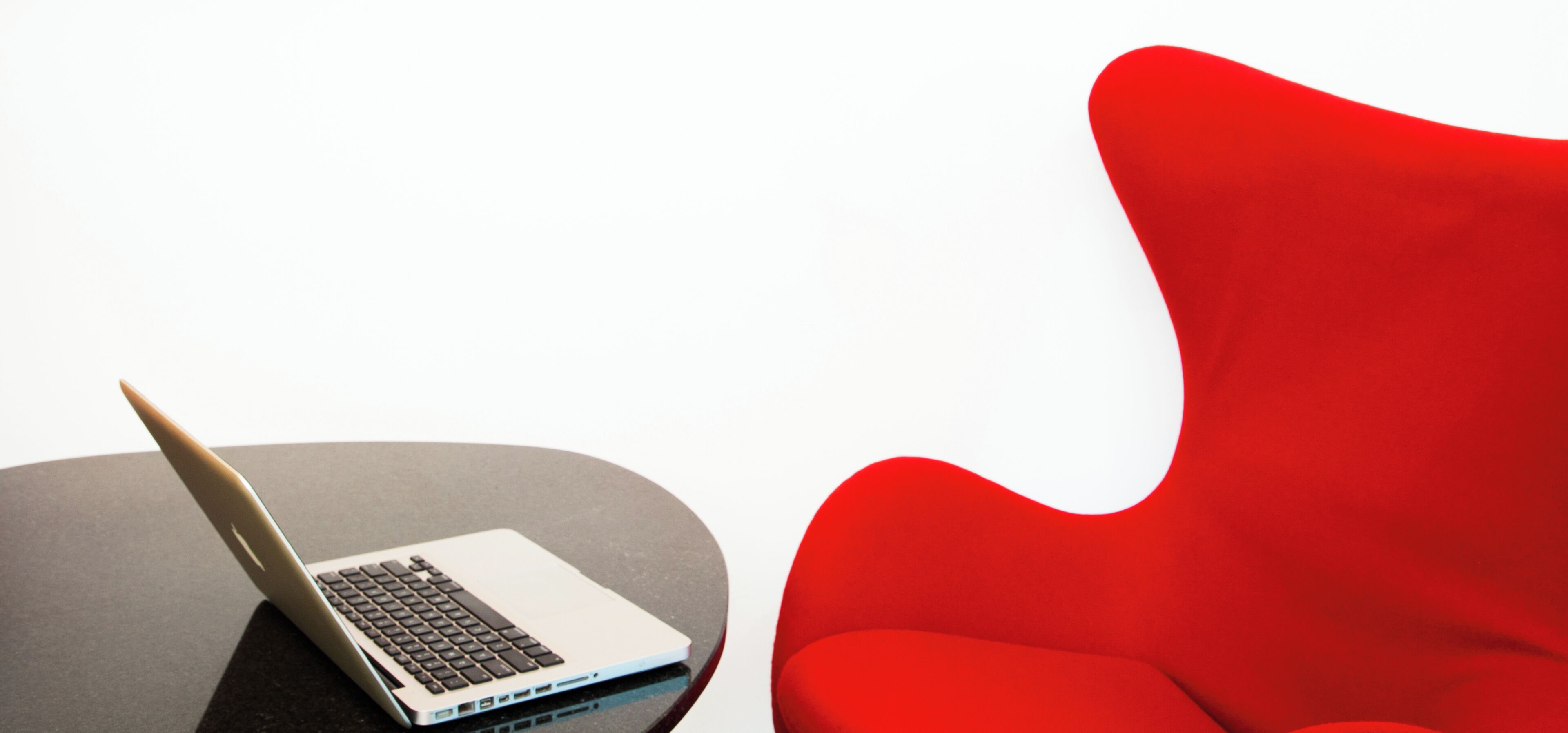 Una computadora portátil sobre una mesa negra, al lado de una silla roja.