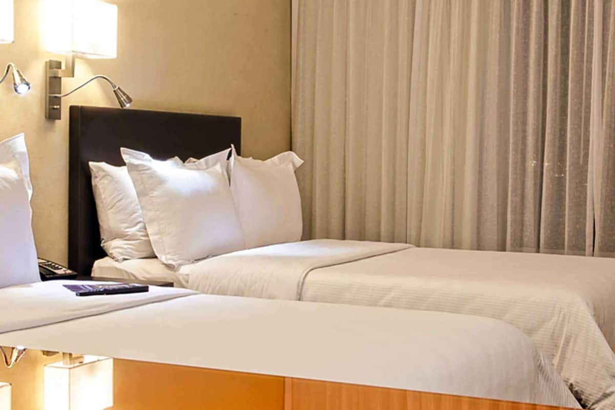 Een hotelkamer met twee bedden, een nachtkastje, een lamp en een raam met gordijnen.