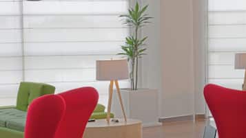 Una habitación moderna con sillas rojas, un sofá verde, una mesita de noche de madera con una lámpara, y un ordenador portátil sobre una pequeña mesa.