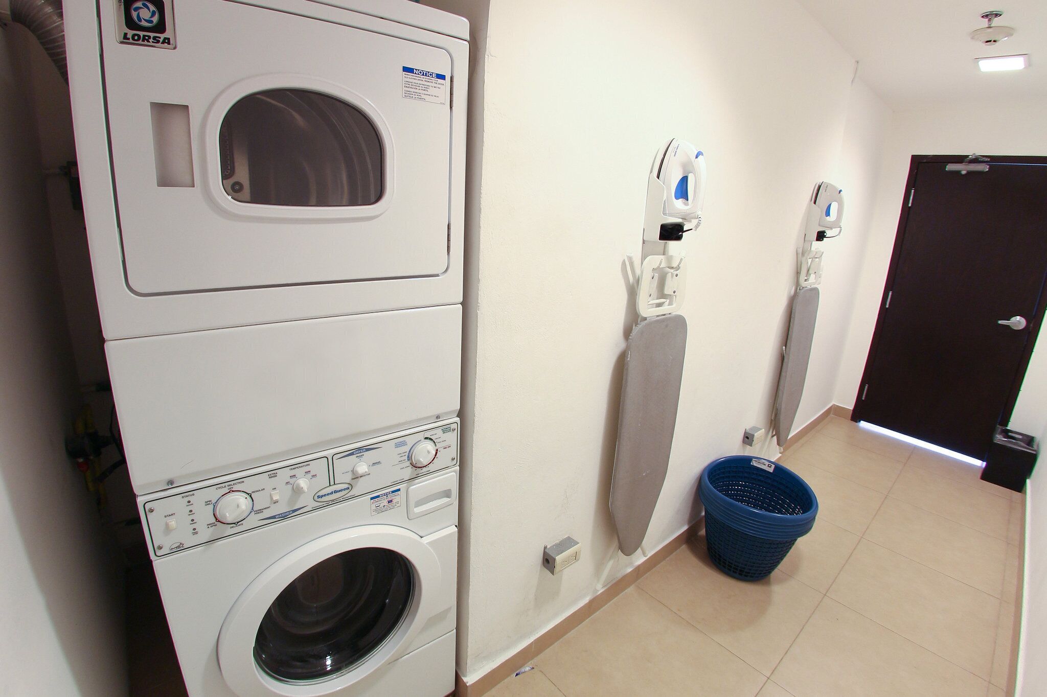 A laundry room with stacked washing machines, a drying rack, and a blue laundry basket.