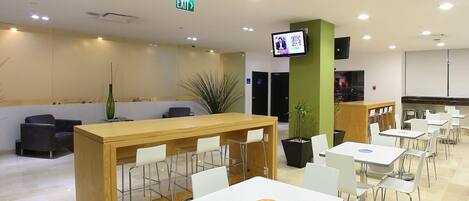 Un espace de restauration moderne comprenant un comptoir d’accueil, des tables et des chaises blanches.