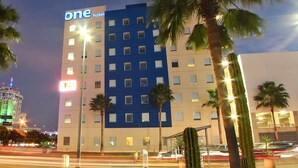 Un hotel con fachada azul y blanca, palmeras y un jardín de cactus.