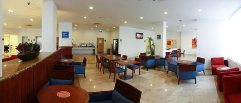 A hotel lobby with seating areas, a reception desk, and a digital screen.