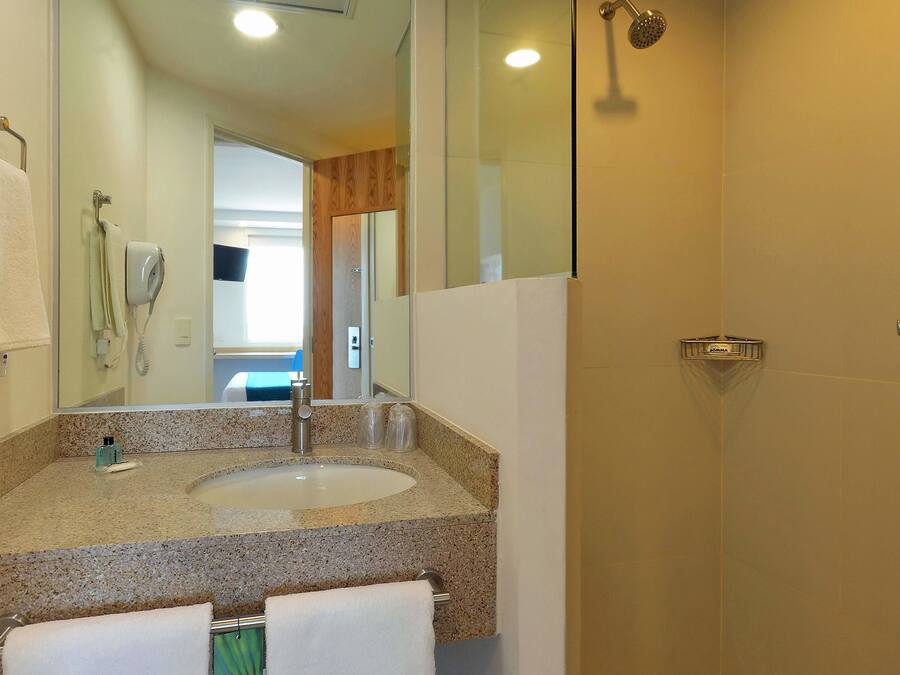 A bathroom with a granite countertop sink, a handheld showerhead, and a glass-enclosed shower.
