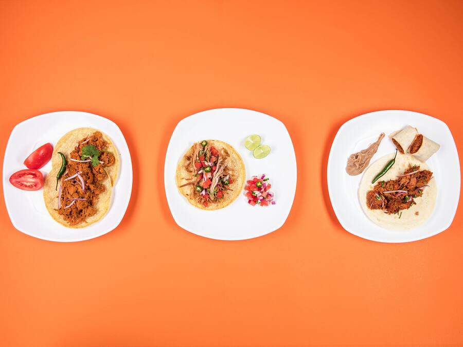 Three white plates with different food items on an orange background.
