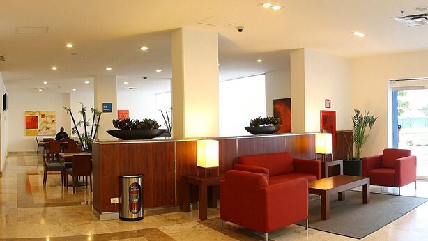 Un hall d’hôtel avec un comptoir d’accueil, un coin salon rouge et une table basse.