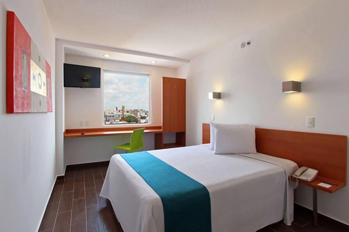 Habitación de hotel con cama, escritorio, silla, ventana y teléfono instalado en la pared.