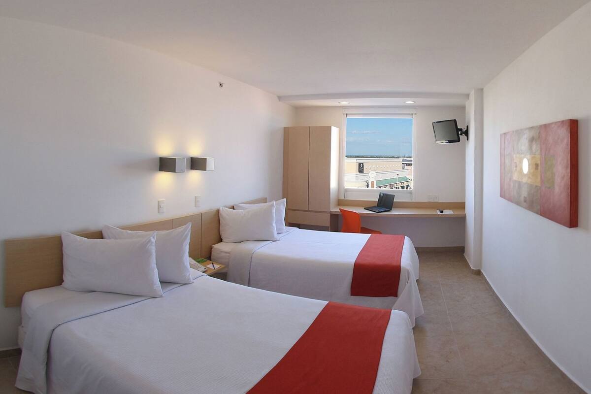 Una habitación de hotel con dos camas, un escritorio, un televisor y una ventana con vistas.