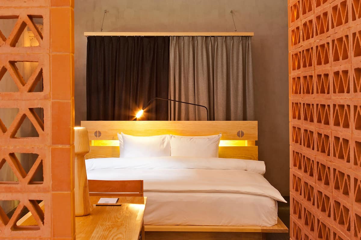 Une chambre d’hôtel bien rangée, avec un lit en bois, une table de chevet et une chaise.