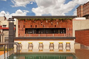 A bar area with a pool, bar stools, and a brick wall with a metal shelf displaying bottles.