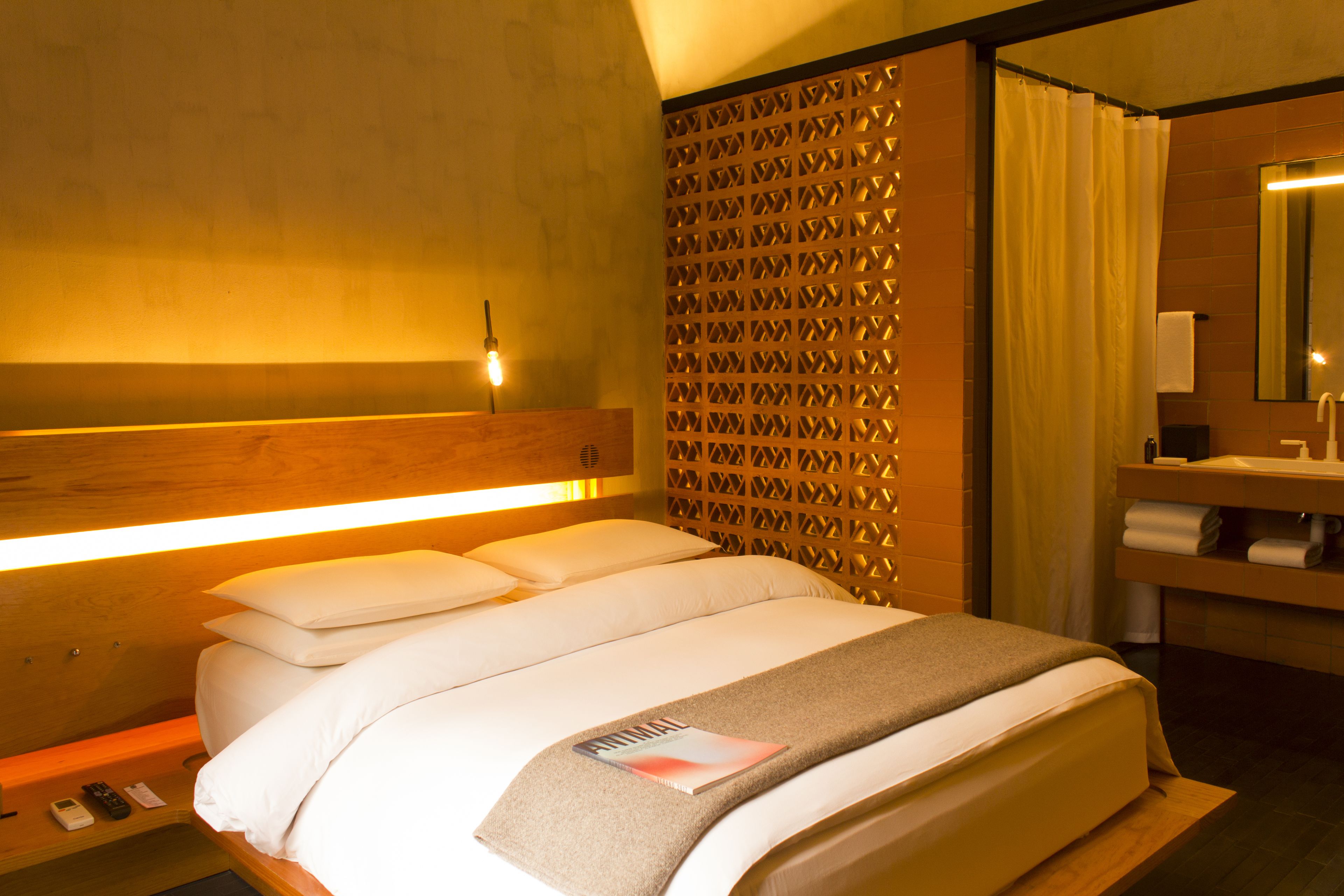 A hotel room with a bed, a nightstand, a mirror, and a bathroom with a sink and towel rack.