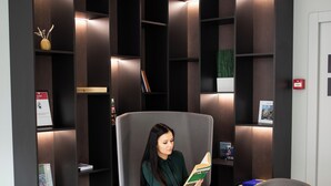 A modern waiting area with a large armchair, two smaller chairs, a small table with a candle, and a bookshelf with various items. - ibis Kaunas Centre (Kaunas)