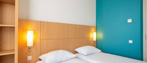 A hotel room with a bed, two bedside tables, a nightstand, and a wall-mounted light fixture.