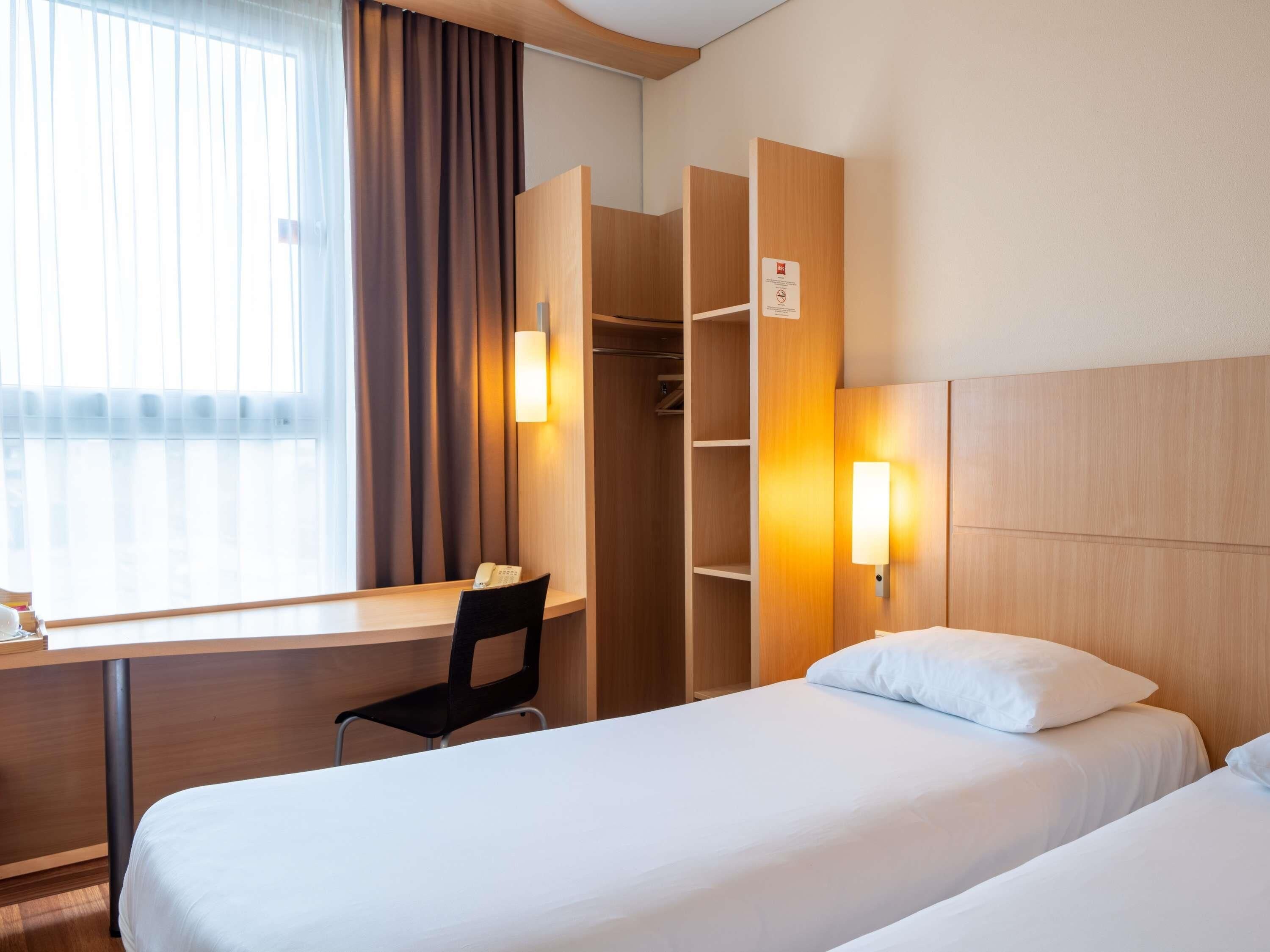 A hotel room with a desk, chair, two beds, and a wardrobe.