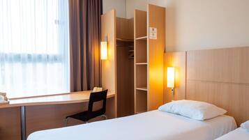 A hotel room with a desk, chair, two beds, and a wardrobe.