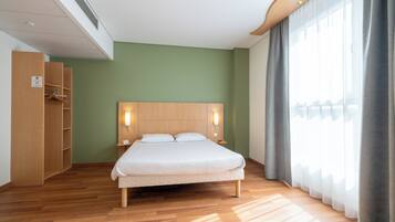 Una habitación de hotel moderna con una cama de madera, un armario y un ventanal con cortinas.