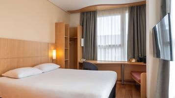 A hotel room with a bed, desk, chair, TV, and a wardrobe.