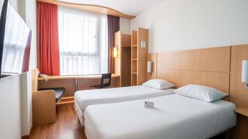 A hotel room with two beds, a desk, a chair, a TV, and a window with curtains.