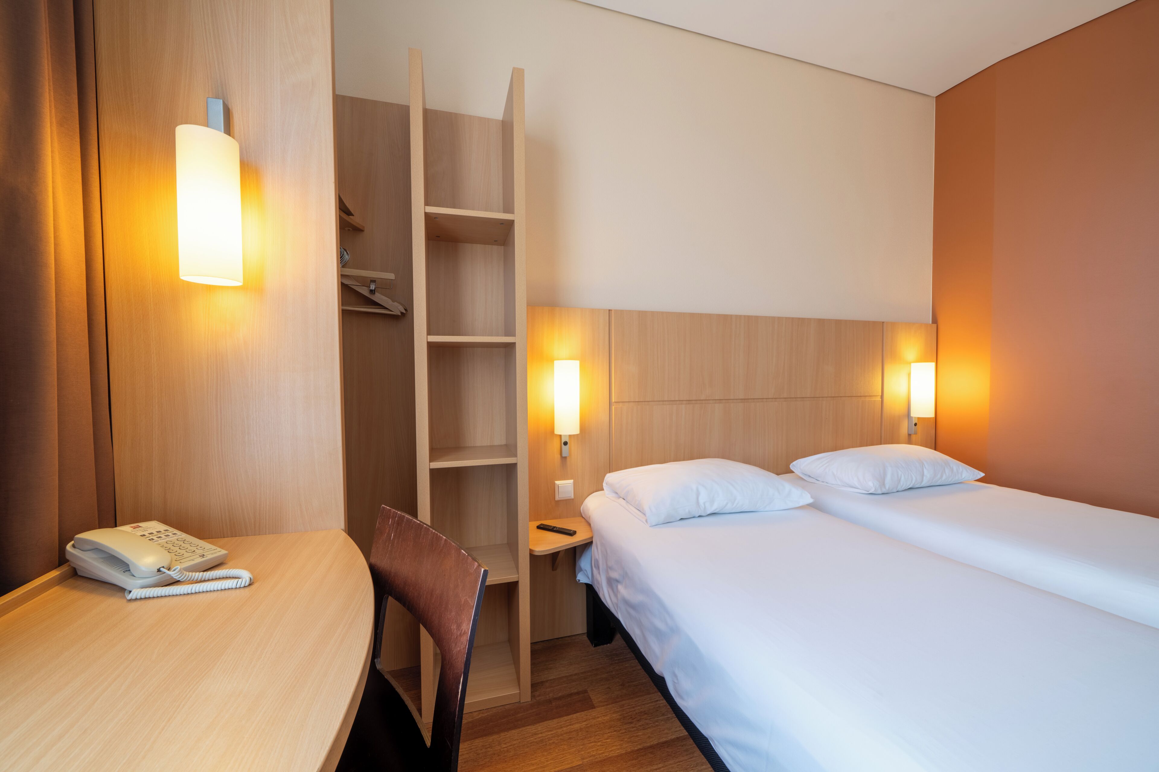 Une chambre d’hôtel comprenant un lit, une table de chevet, un téléphone, une chaise et une armoire en bois.