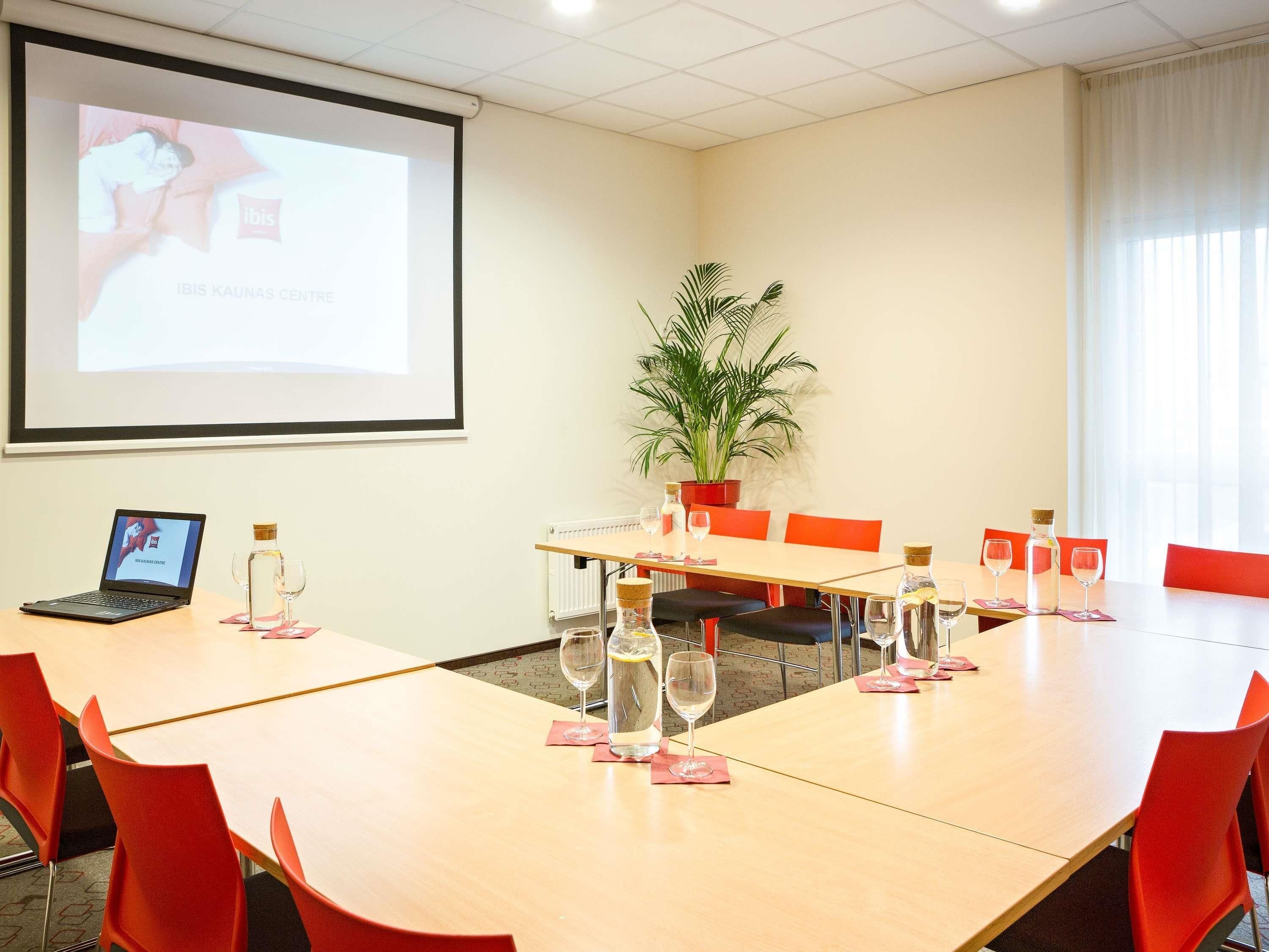 Een vergaderruimte met een projectiescherm, een laptop, een potplant en een tafel gedekt voor een vergadering.
