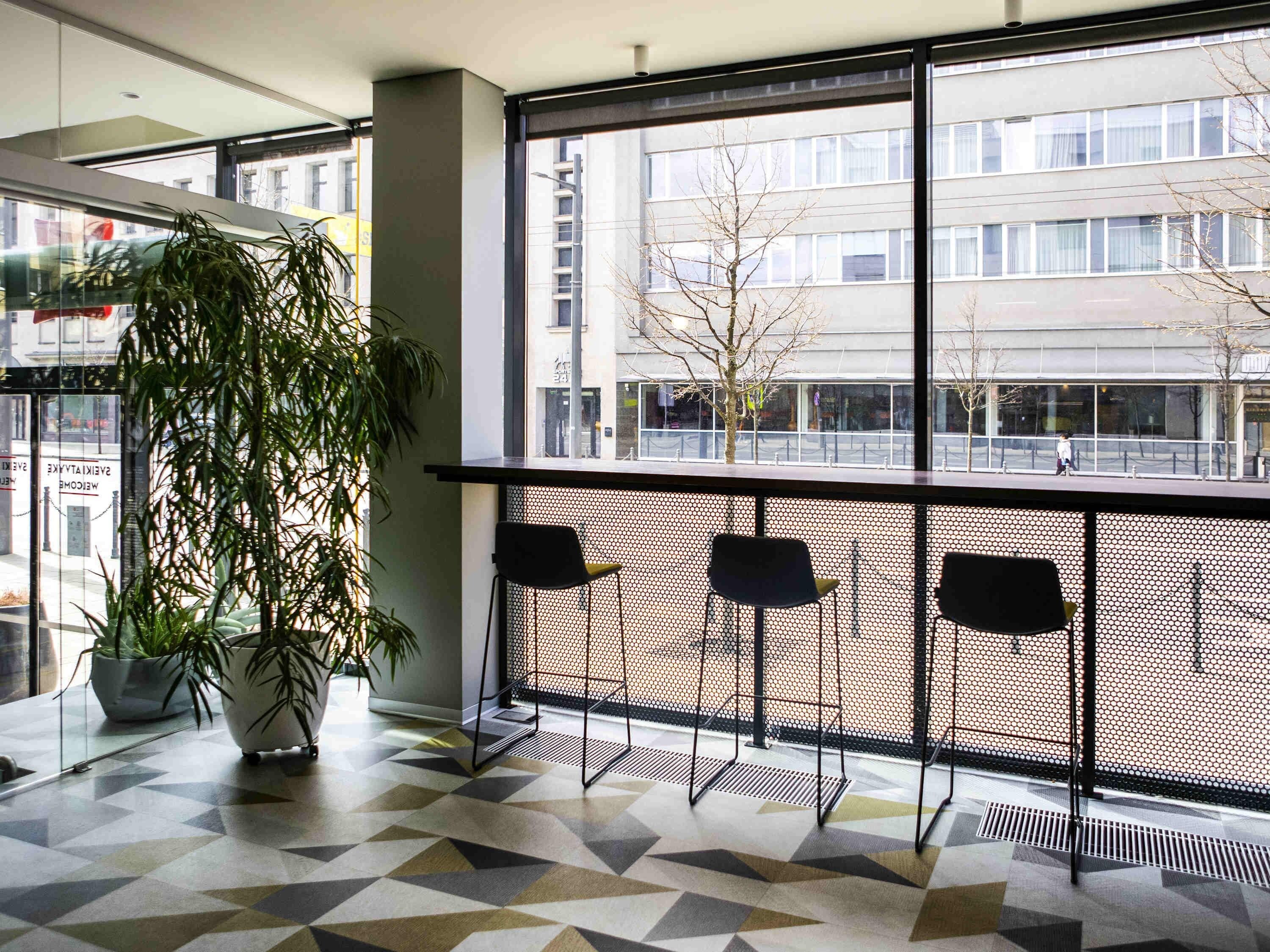 A modern interior with a geometric patterned floor, a large window with a view of a cityscape, and a potted plant.