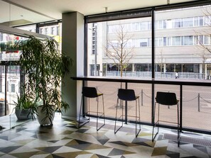A modern interior with a geometric patterned floor, a large window with a view of a cityscape, and a potted plant. - ibis Kaunas Centre (Kaunas)