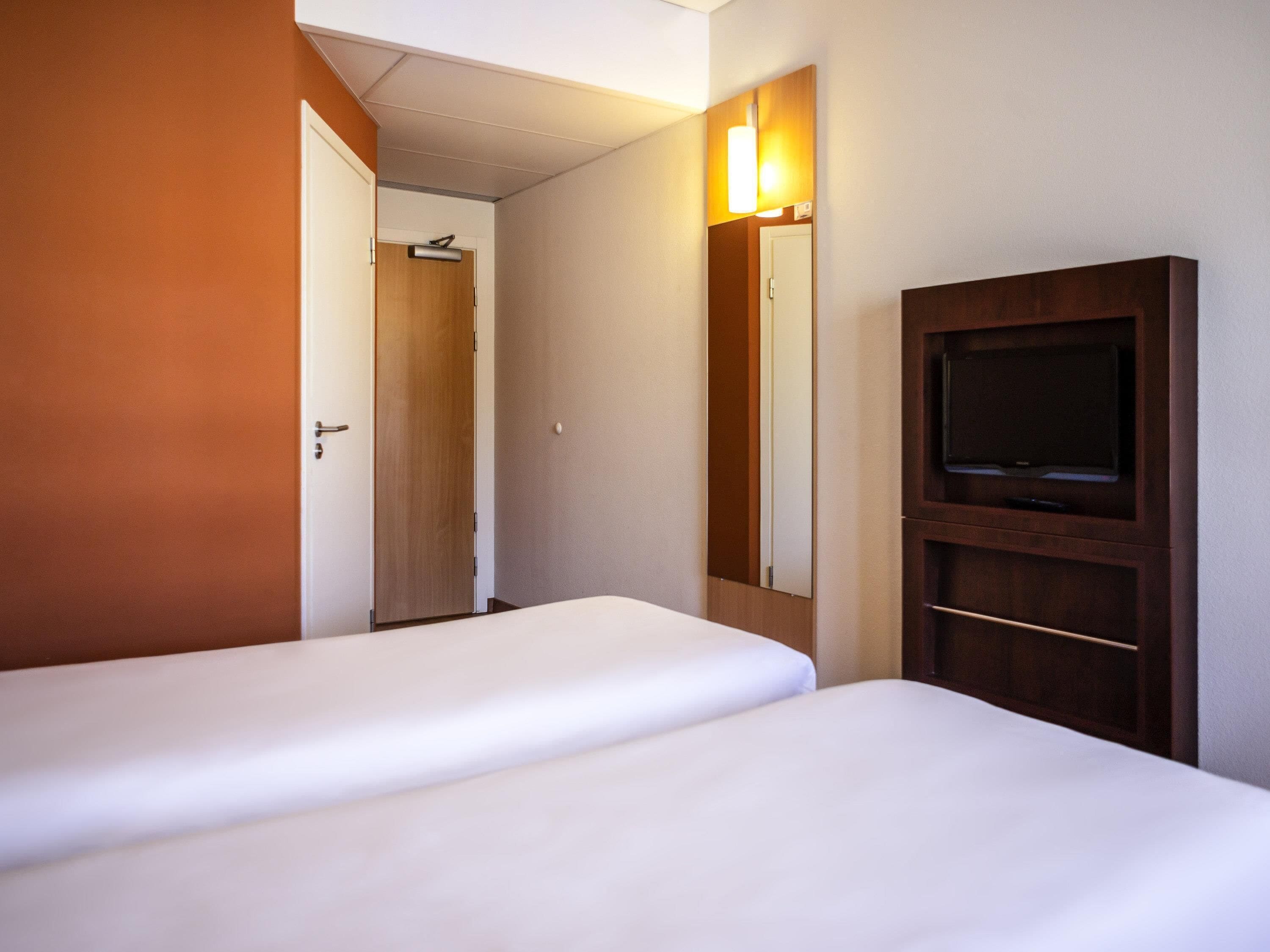A hotel room with two beds, a television, and a mirror.
