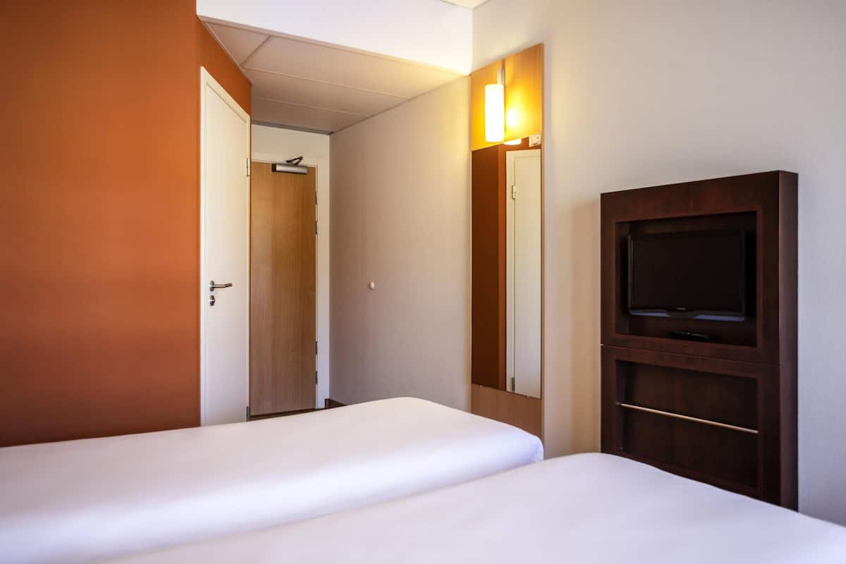 A hotel room with two beds, a television, and a mirror.