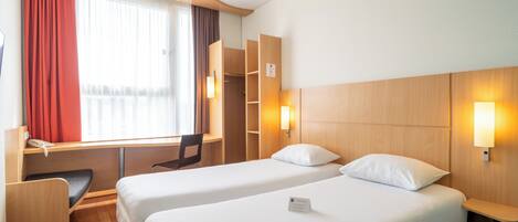 Una habitación de hotel con dos camas, un escritorio, una silla y un armario.