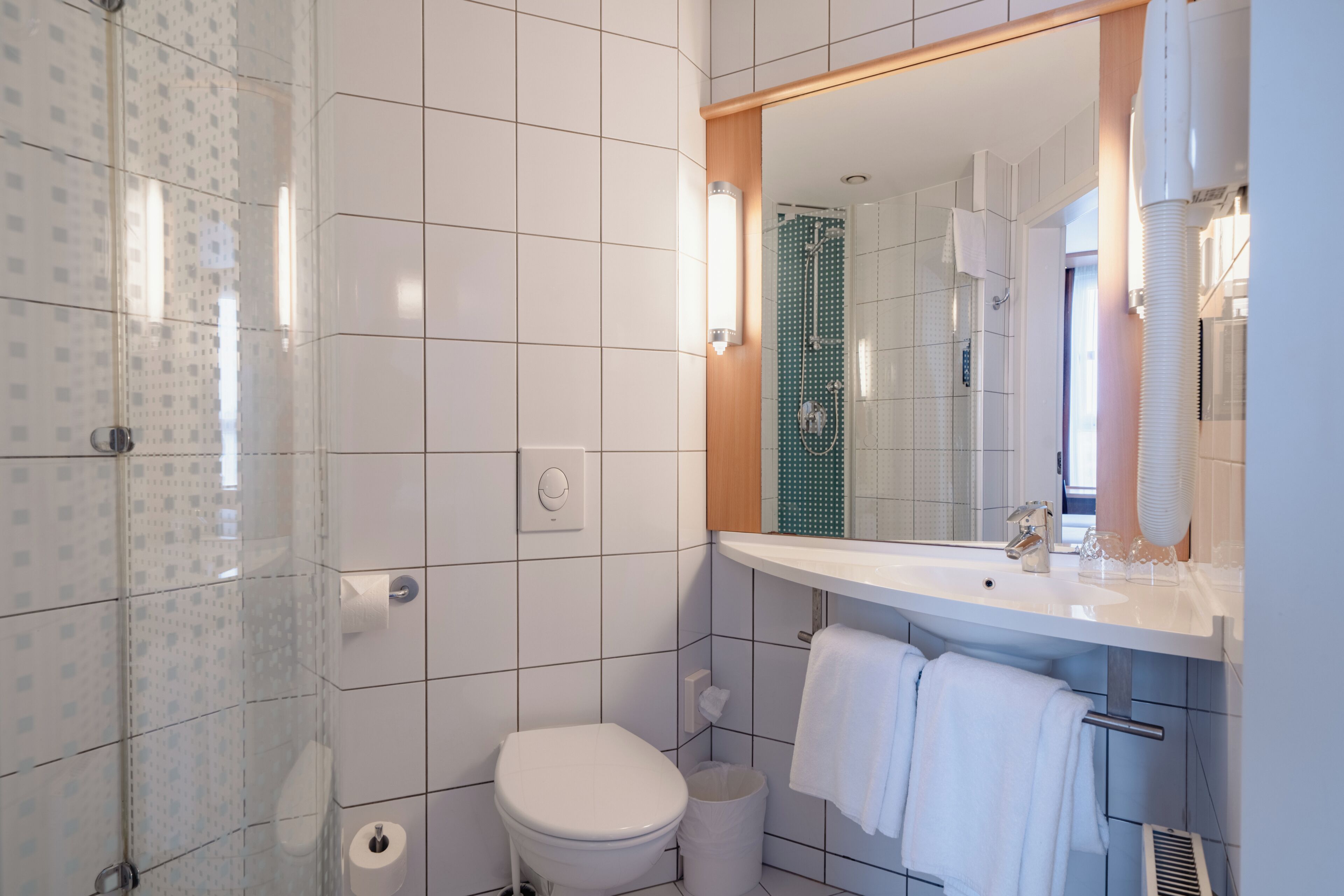 A modern bathroom with a toilet, sink, mirror, and shower.