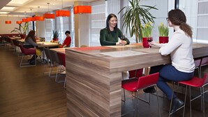 A modern dining area with wooden tables, red chairs, and orange pendant lights. - ibis Kaunas Centre (Kaunas)