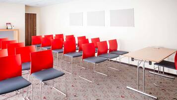 A conference room with rows of red chairs, a projector, and a wooden desk.