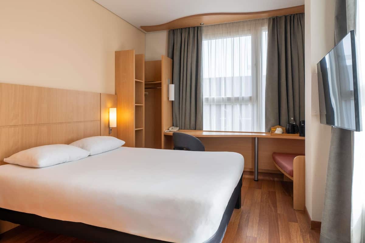 A hotel room with a bed, desk, chair, TV, and a wardrobe.