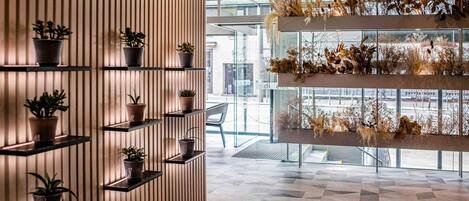 A modern interior with vertical wooden slats, multiple potted plants on shelves, and a geometric patterned floor.