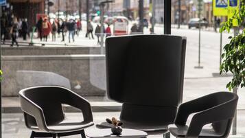 A modern interior with two black chairs, a small table, and a large window offering a view of a busy street outside.