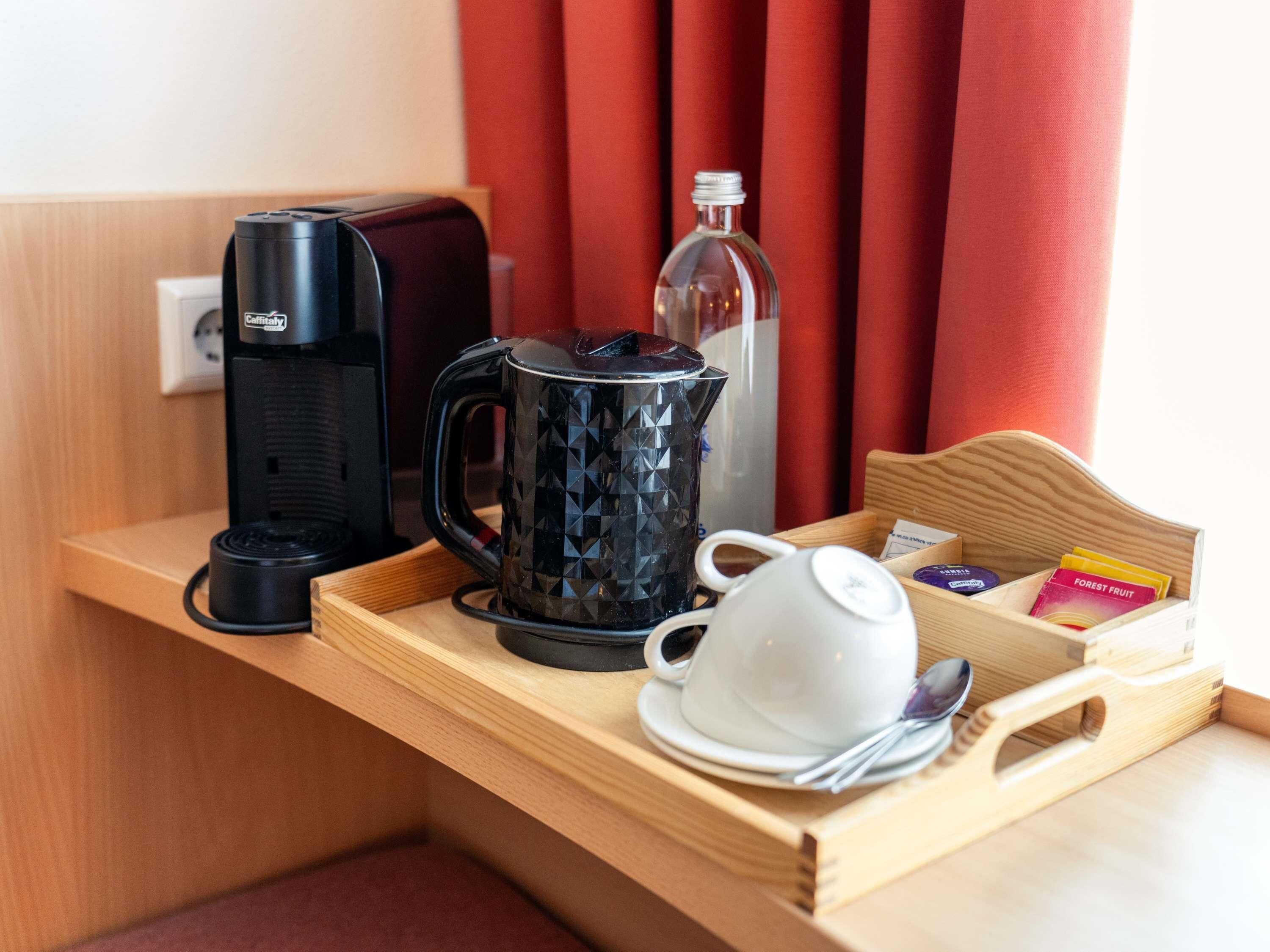A tray with a coffee maker, a glass carafe, a white cup, and a box of tea bags.