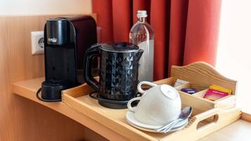 A tray with a coffee maker, a glass carafe, a white cup, and a box of tea bags.